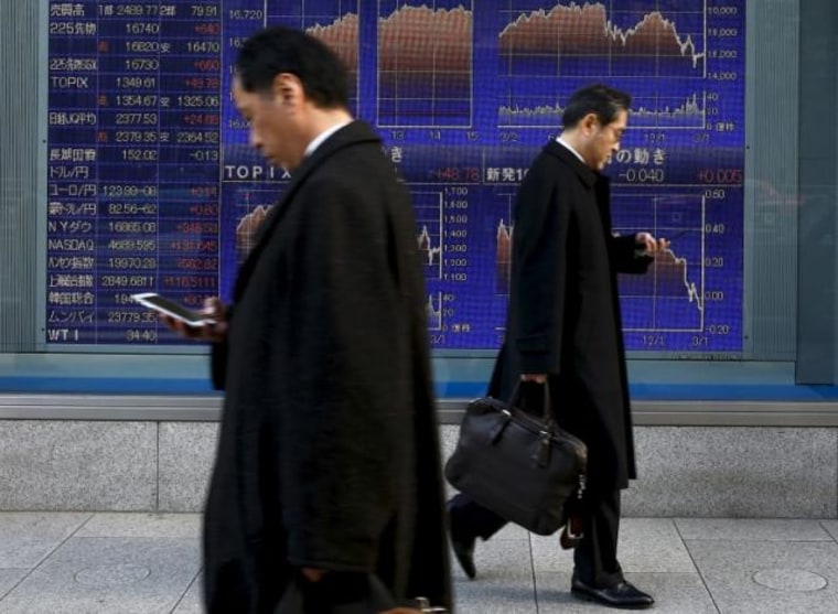 Men walk past an electronic board showing market indices outside a brokerage in Tokyo