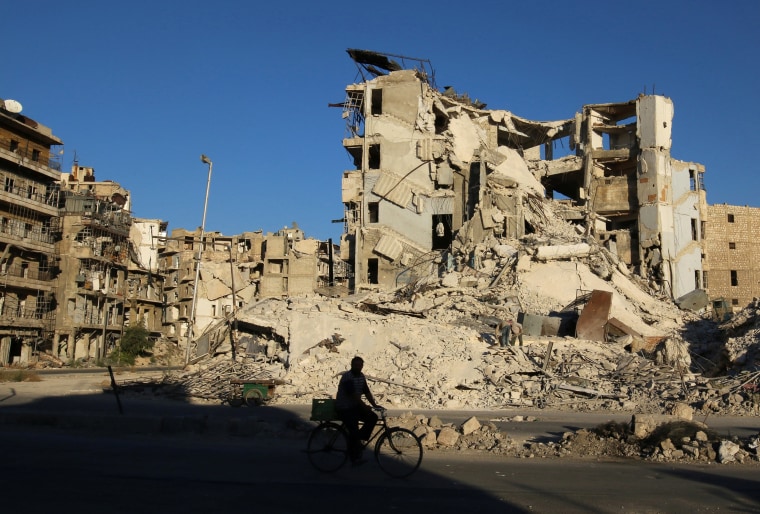 Image: A man rides a bicycle past damaged buildings in the rebel-held Tariq al-Bab neighborhood of Aleppo