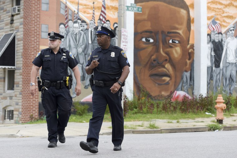 Image: Baltimore police walk near a mural depicting Freddie Gray