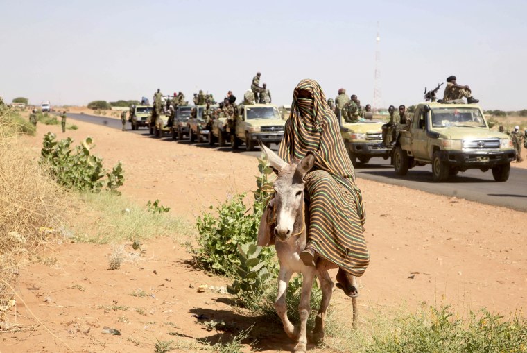 A woman rides a donkey past a convoy of government troops in the North Darfur region of Sudan on Nov. 20, 2014. 