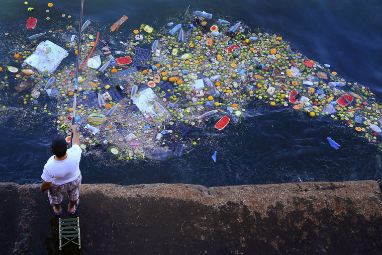 Image: A man holds a fishing rod as floating trash hits the coastline of the Mediterranean Sea in Beirut