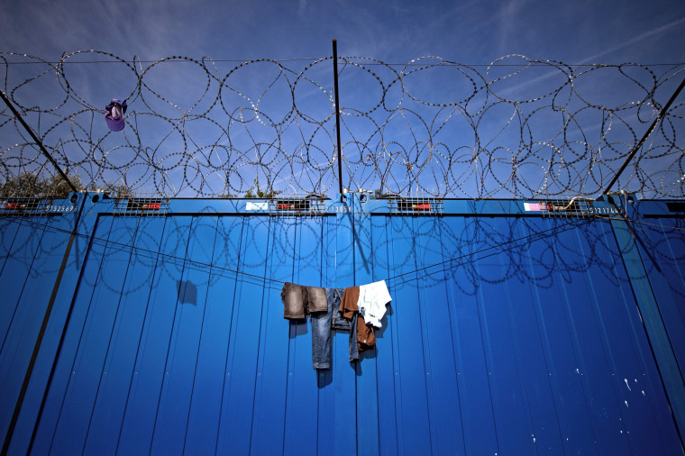 Image: Clothes hang on the barbed wires at a makeshift refugee and migrants camp