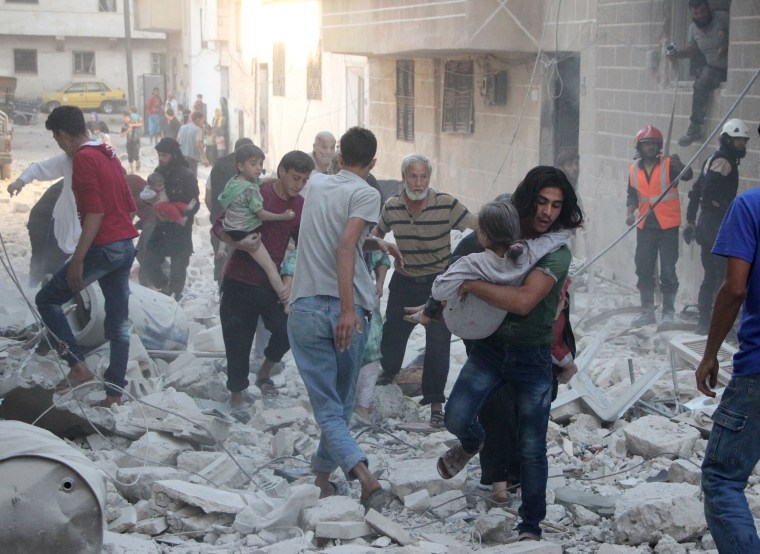 Image: Syrian men carry injured people amid the rubble of destroyed buildings in Idlib