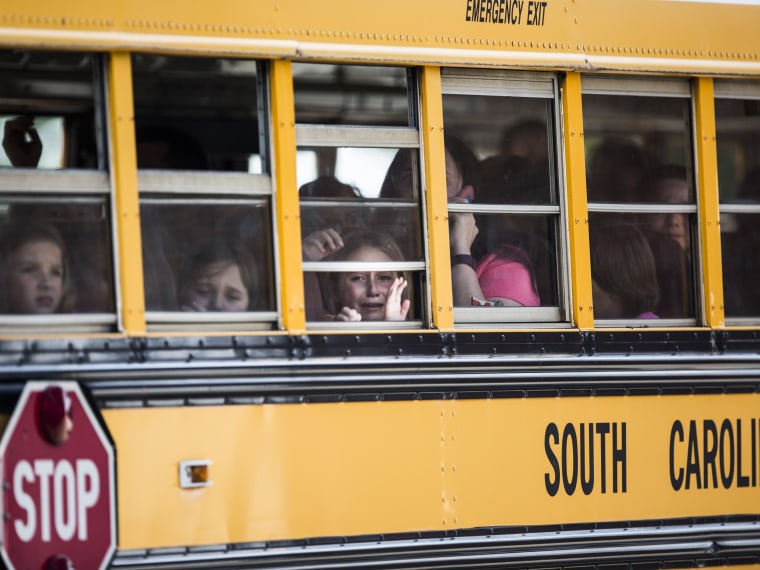 Image: A student looks out of the window of a school bus as she and her classmates are transported after a shooting