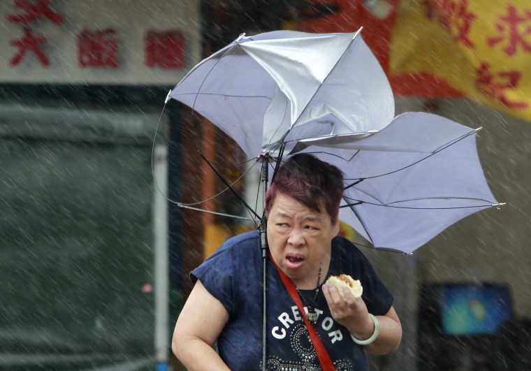 Image: A woman eats while struggling with her umbrella against powerful gusts of wind generated by typhoon Megi