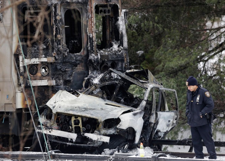 Image: A police officer looks at an SUV that was crushed at the front of a Metro-North train