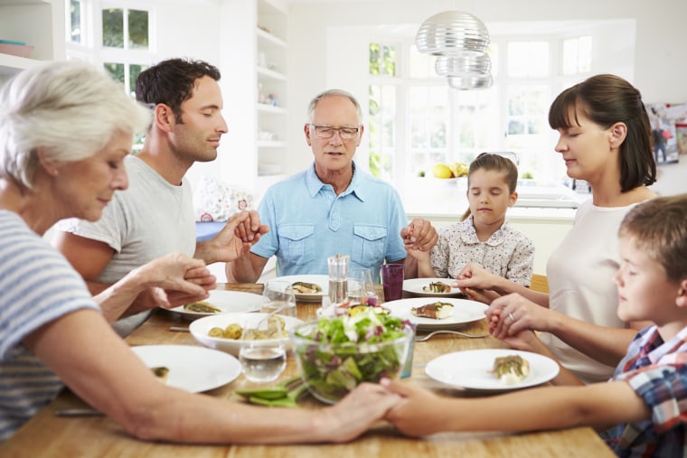 family saying grace at dinner table