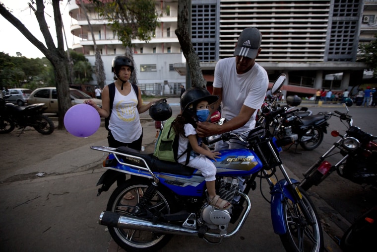 In this Sept. 19, 2016 photo, Maykol Pacheco, places a helmet on his daughter Ashley as they prepare to ride away from the University Hospital in Caracas, Venezuela.