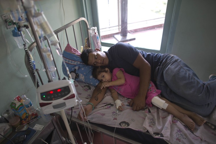 In this Aug. 11, 2016 photo, 3-year-old Ashely Pacheco rests with her father Maykol Pacheco in her hospital bed at the University Hospital in Caracas, Venezuela.