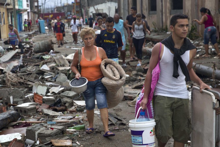 Image: People carry some of their belongings through the rubble of a street