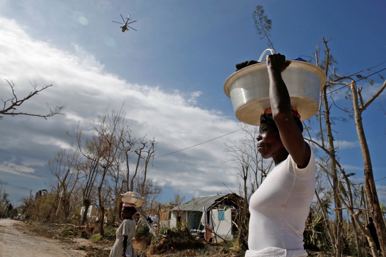 Image: Women carry their belongings as a helicopter flies in the sky, after Hurricane Matthew hit Jeremie