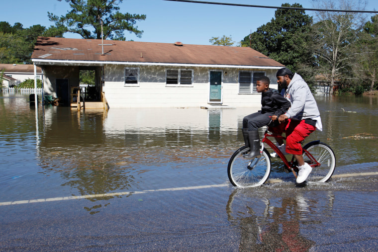 Image: Residents ride their bicycle past a flooded house after Hurricane Matthew hit Lumberton