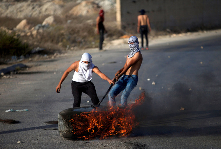 Image: Palestinian protesters drag a burning tyre during clashes with Israeli troops in the West Bank town of Al-Ram