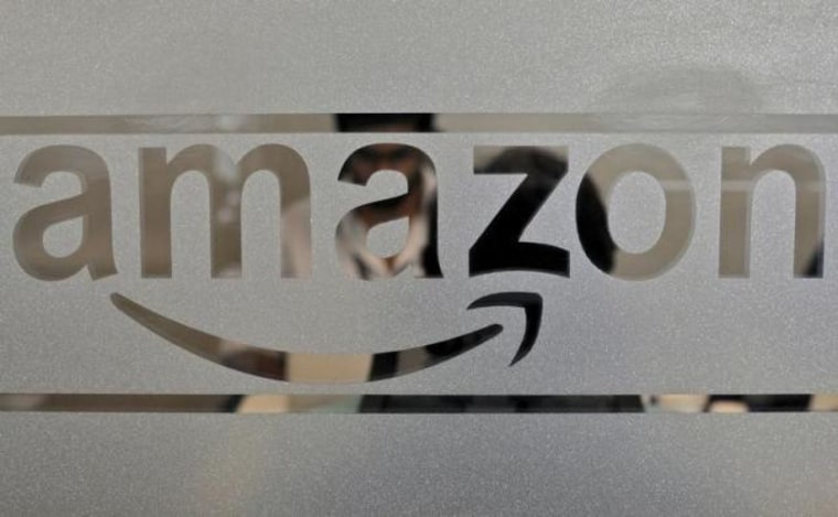 Employees of Amazon India are seen behind a glass bearing the company's logo inside its office in Bengaluru