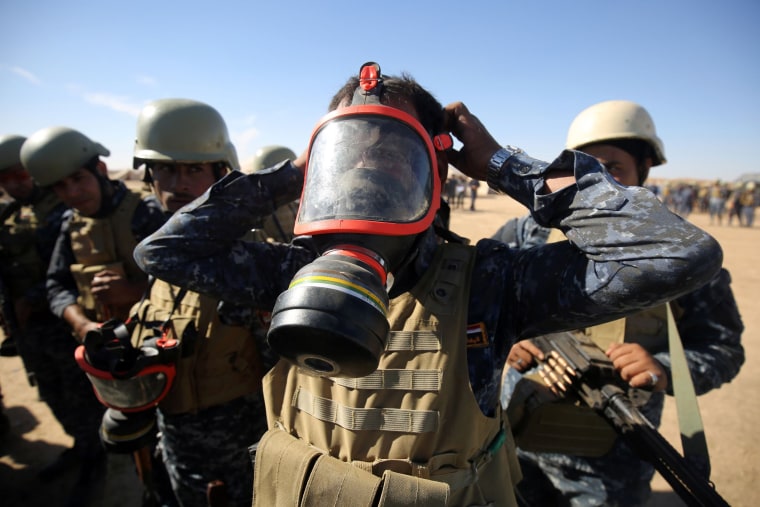Image: An Iraqi policeman tries on a gasmask at the Qayyarah military base