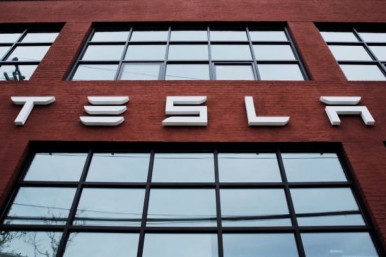 A Tesla logo hangs on a building outside of a Tesla dealership in New York