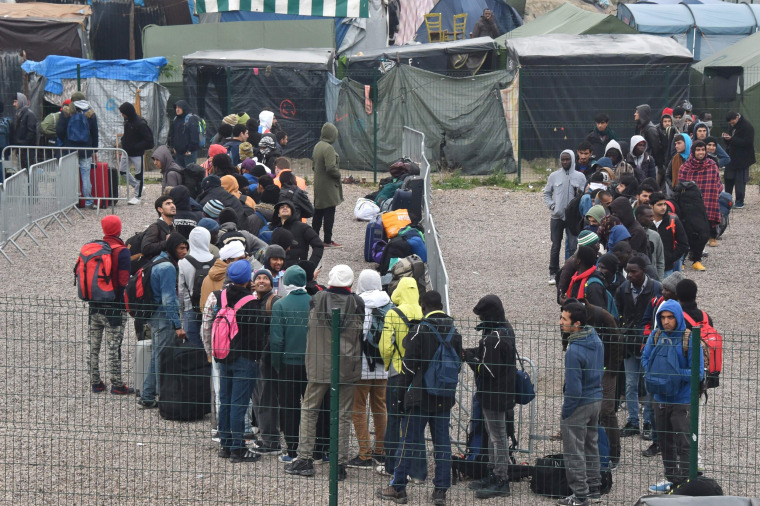 Image: Migrants queue outside a hangar where they will be sorted into groups