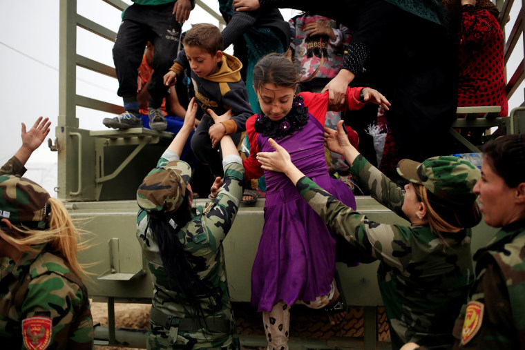 Image: Kurdish female Peshmerga soldiers help newly internally displaced children jump down from the truck upon their arrival at Al Khazar camp near Hassan Sham, east of Mosul