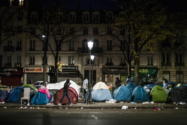 Image: A migrant passes by tents in a makeshift camp in the 19th district of Paris, Thursday.