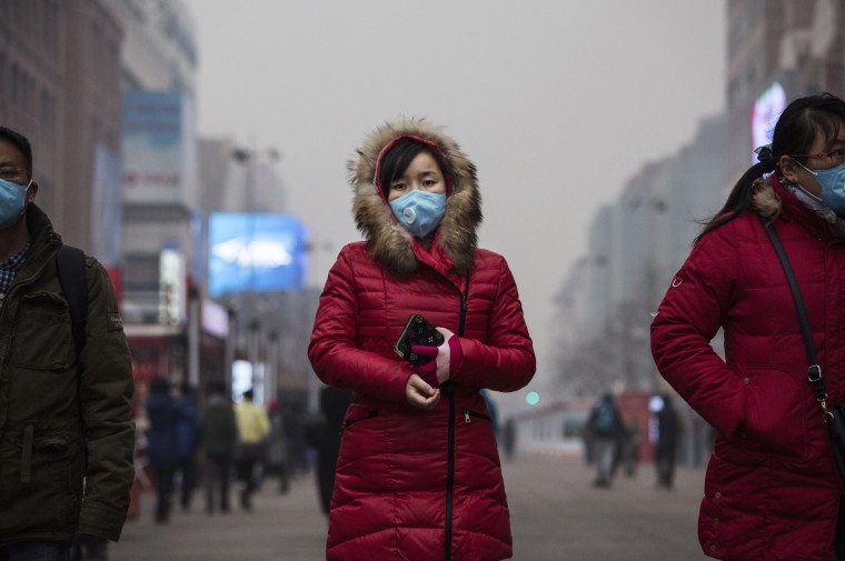 Image:  A Chinese woman wears mask to protect agains pollution as she walks through a shopping area in heavy smog on December 8, 2015 in Beijing, China.
