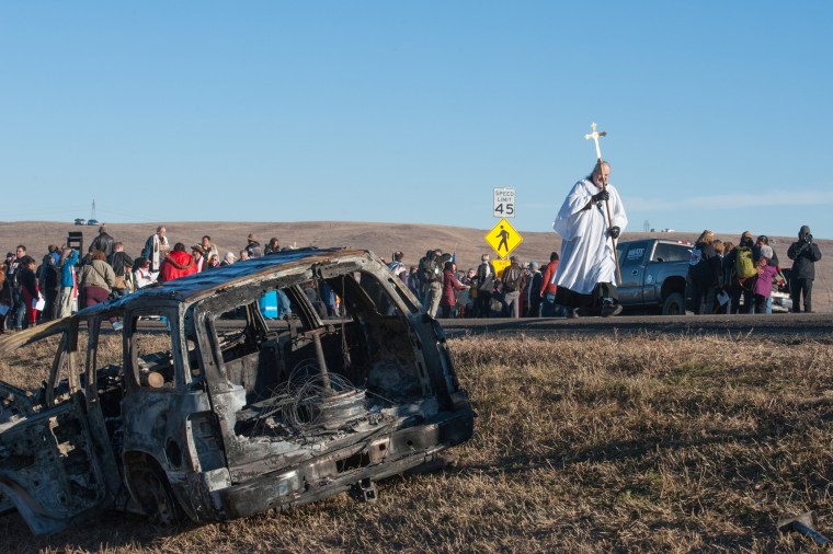 Image: A member of the clergy walks past a burnt out car during a protest of the Dakota Access pipeline on the Standing Rock Indian Reservation near Cannonball