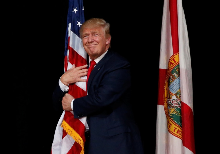 Image: Trump hugs a U.S. flag as he comes onstage to rally with supporters in Tampa, Florida
