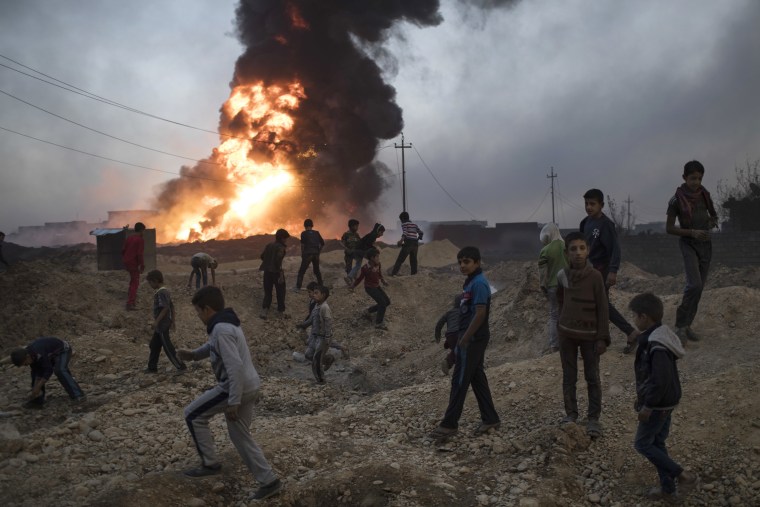 Image: Children play next to a burning oil field in Qayara, south of Mosul