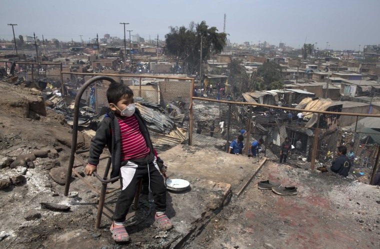 A boy wearing a mask as protection from smoke caused by an early morning fire, plays with the shell of a charred chair, in the shantytown known as Cantagallo, in Lima, Peru, Friday, Nov. 4, 2016.