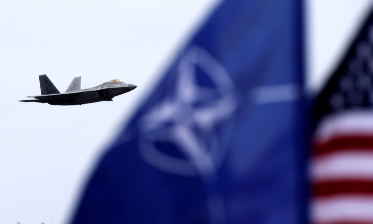 Image: NATO and U.S. flags flutter as U.S. Air Force F-22 Raptor fighter flies over the military air base in Lithuania