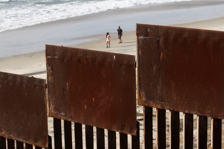 Image: Tourists are seen behind a fence separating Mexico and the United States