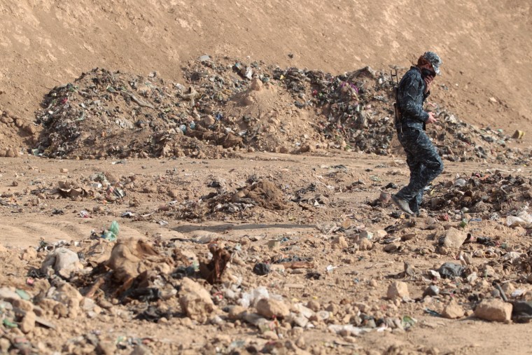 Image: A member of the Iraqi forces check a mass grave they discovered in the Hamam al-Alil area