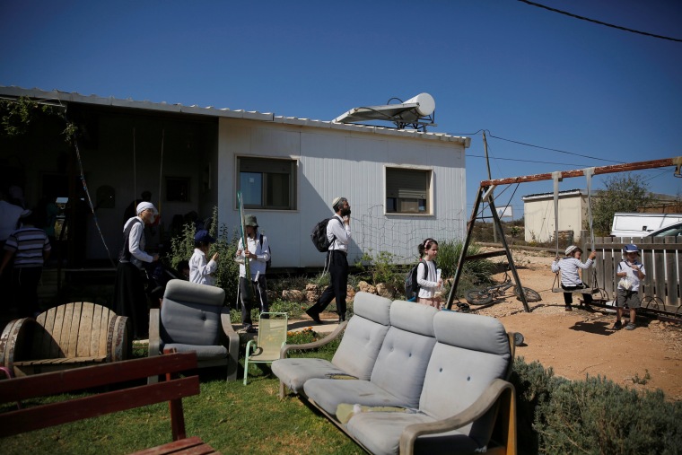 Image: Visitors walk in a yard near a home in the Jewish settler outpost of Amona