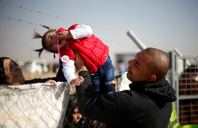 Image: A displaced Iraqi man, who fled the Islamic State stronghold of Mosul, holds his daughter to be seen by her grandmother through a fence at Khazer camp