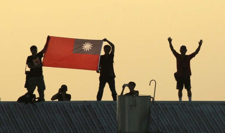 Locals on a warehouse rooftop display the national flag while watching Taiwan fighter jets practice emergency landing drills on a closed section of highway during the annual Han Kuang military exercises in  2014, in Chiayi, central Taiwan.