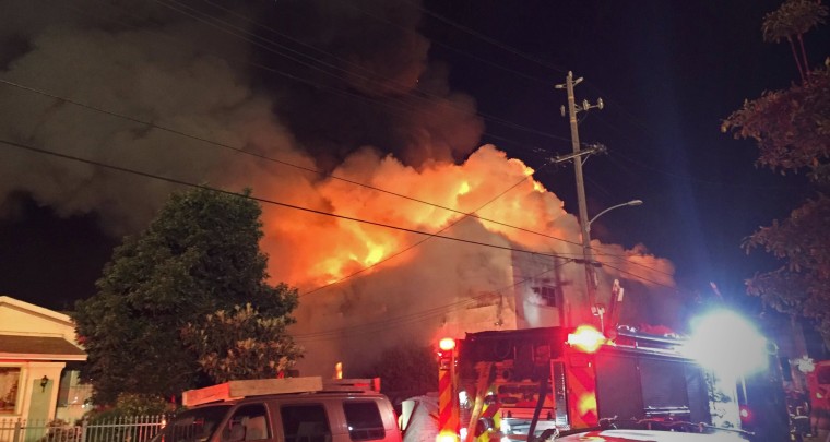 Image: Flames rise from the top of a warehouse, which caught fire during a dance party in Oakland