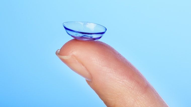 Contact lens on finger on blue background