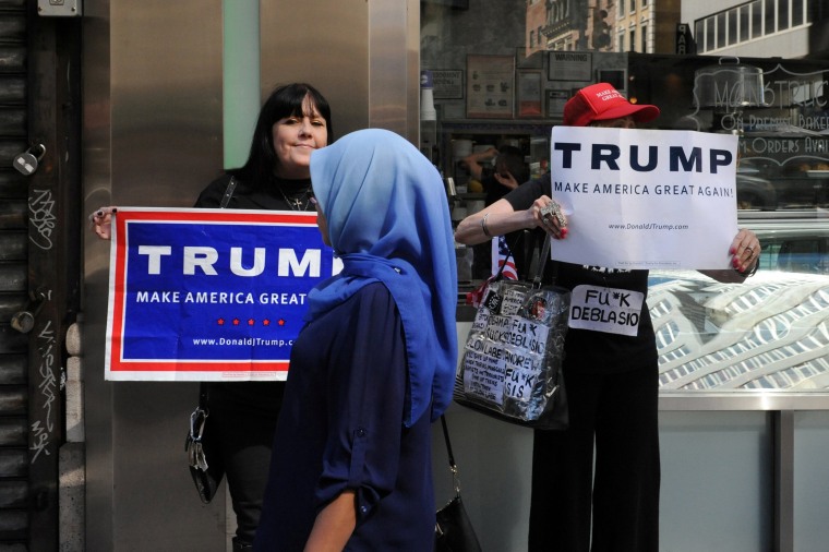Image: A woman wearing a Muslim headscarf walks past people holding Donald Trump signs