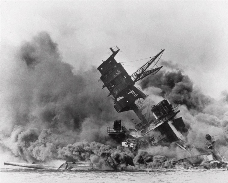 Image: The battleship USS Arizona belches smoke as it topples over into the sea.