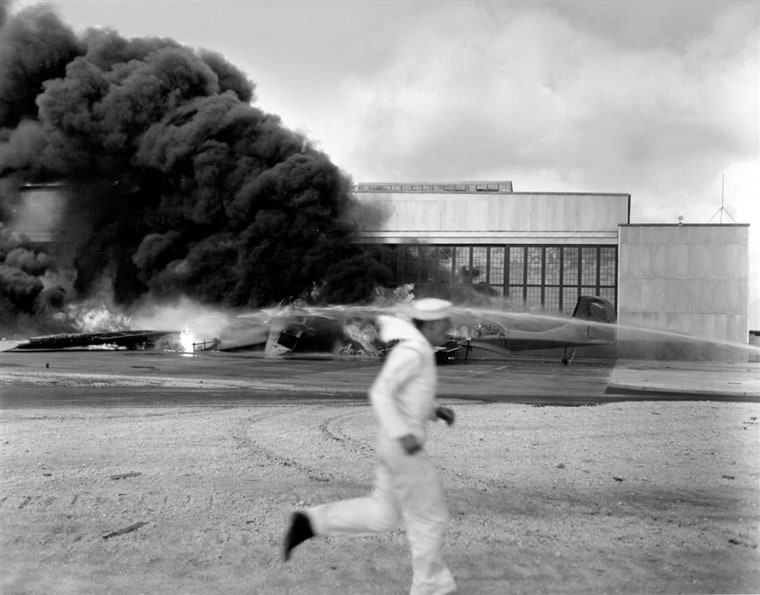 Image: A sailor runs for cover past flaming wreckage hit by dive bombers that had already blasted Pearl Harbor and Hickam Field.
