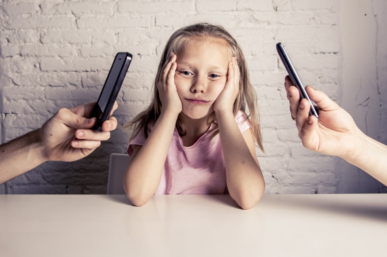Image: A child sits between two people holding phones