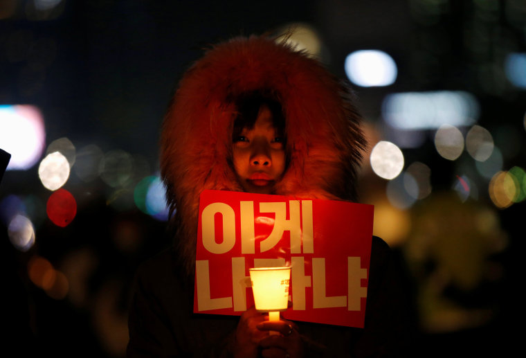 Image: A woman holds a candle light and a slogan at a protest calling South Korean President Park Geun-hye to step down in Seoul