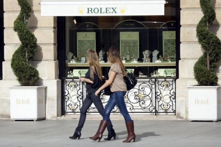 Women walk past a window display of luxury goods maker Rolex in Paris' Place Vendome