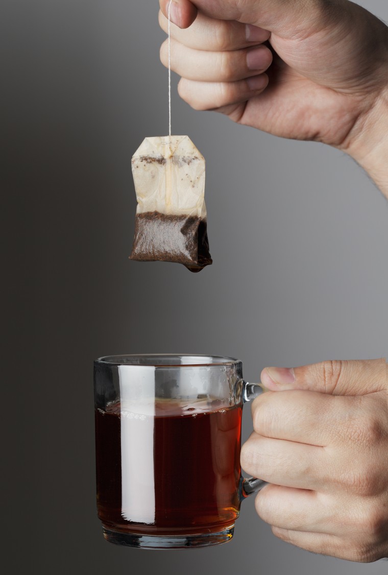 Hand lifting a used tea bag from a glass tea mug.