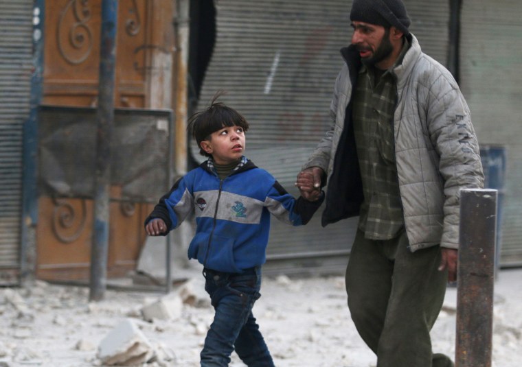 Image: A man holds the hand of a boy as they flee deeper into the remaining rebel-held areas of Aleppo