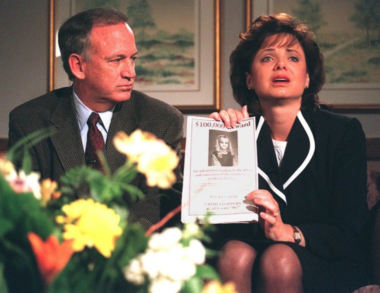 Image: John Ramsey looks on as his wife Patricia holds up