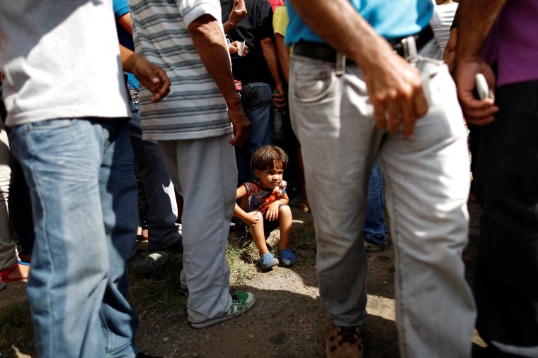 Image: Emmanuel Cuauro seats on the sidewalk next to his mother Zulay Pulgar, as they make a line outside the hardware store to buy cement and re-sell it in Punto Fijo