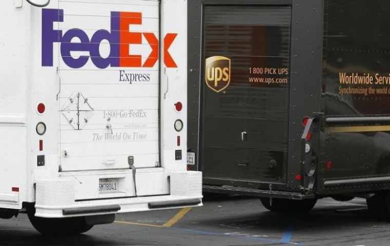 A FedEx truck is parked next to a UPS truck as both drivers make deliveries in downtown San Diego