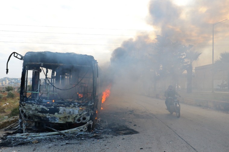 Image: A man on a motorcycle drives past burning buses