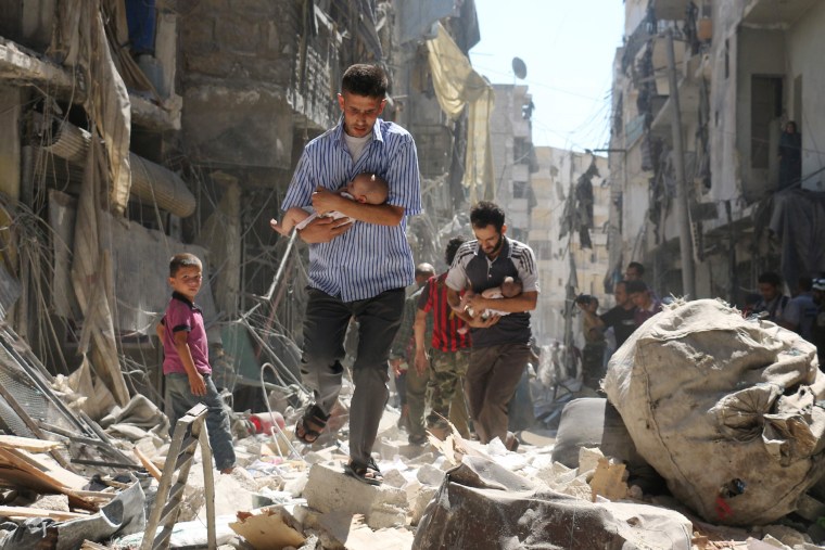 Image: Syrian men carrying babies make their way through the rubble of destroyed buildings