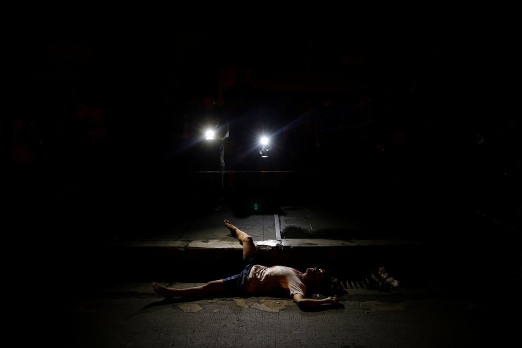 Image: The body of a man killed by unknown gunmen is lit by lights from TV cameras in Manila